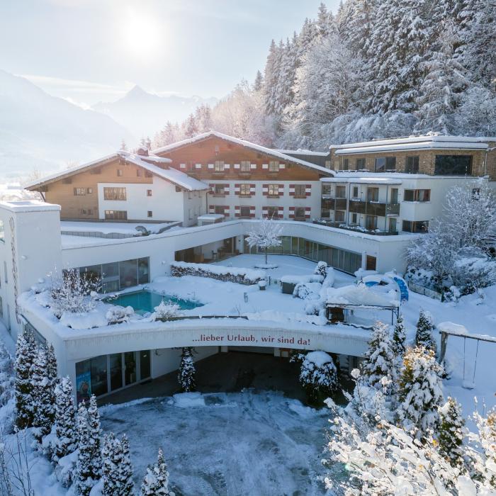 Ein charmantes Berghotel eingebettet in eine verschneite Alpenlandschaft. Die Fassade ist von winterlichen Bäumen und einer glitzernden Schneedecke umgeben. Ein beheizter Außenpool und sonnige Panorama-Terrassen bieten einen atemberaubenden Blick auf die Berge. Perfekt für Erholung und Winterurlaub.